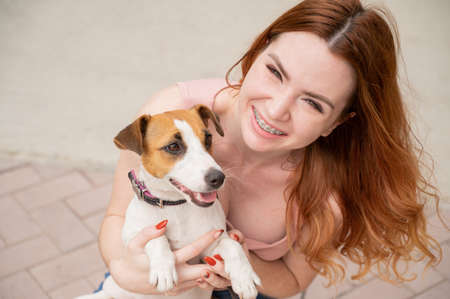 Young red-haired woman is cuddled with a jack russell terrier dog outdoors.の写真素材