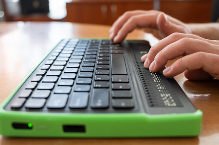 A blind man uses a computer with a Braille display and a computer keyboard. Inclusive device.