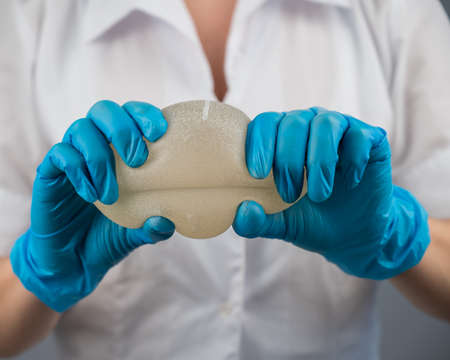 A plastic surgeon demonstrates the strength of silicone breast implants by squeezing them.の写真素材