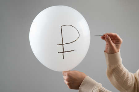 Caucasian woman pops a balloon with a ruble inscription with a needle.の写真素材