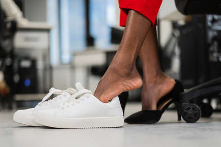 African woman changing from high heels to sneakers in the office. Tired legs.の写真素材