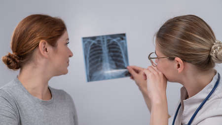 The doctor consults a caucasian woman and comments on the x-ray of the lungs.