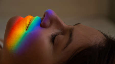 Close-up portrait of caucasian woman with ray of rainbow light on her face.の写真素材