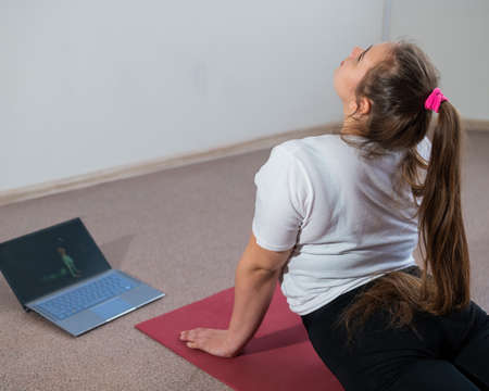 A chubby young woman is watching an online fitness lesson on a laptop. Distance sports training.