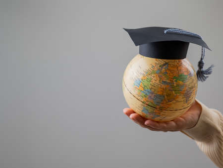 Woman holding a globe wearing a graduation cap.の写真素材