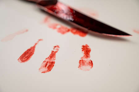 Bloody knife and hand prints in blood on a white table.の写真素材
