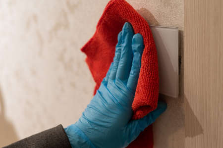 Caucasian woman in gloves wipes touch switch with napkin.