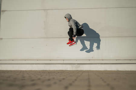 Caucasian man in hoodie jumping high with hands on knees outdoors.