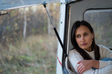 Portrait of a caucasian woman looking out of a trailer window. Travel in a camper in autumn.の写真素材