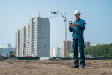 A man in a helmet and overalls controls a drone at a construction site. The builder carries out...