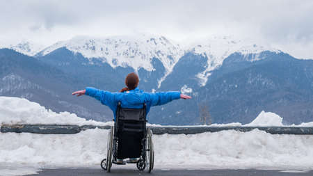 Rear view of a woman in a wheelchair spread her arms to the side like wings in the mountains in...