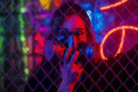 Caucasian woman in a gas mask behind a fence in a neon studio.の写真素材