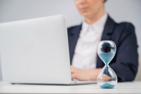Business woman keeps track of time on an hourglass while working.の写真素材
