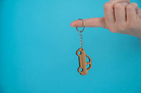 Womans hand holding a wooden keychain in the shape of a car on a blue background.の写真素材
