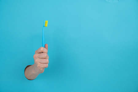 A womans hand sticks out of a blue paper background and holds a toothbrush.