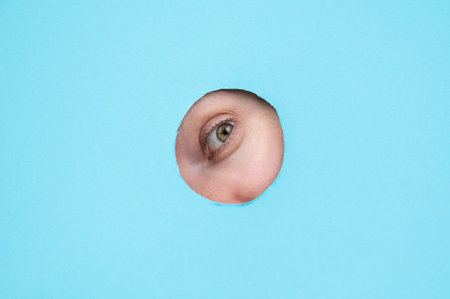 Woman peeking out of hole in blue paper background.の写真素材