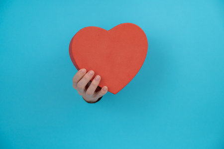 A womans hand with a heart-shaped gift box sticks out of a blue paper background.の写真素材