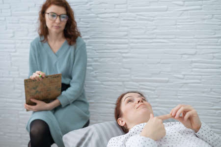 A middle-aged woman lies on a couch and talks to a psychologist.の写真素材