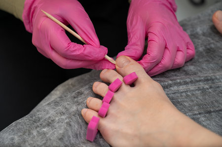 Pedicure master cleans clients toes with wooden stick.