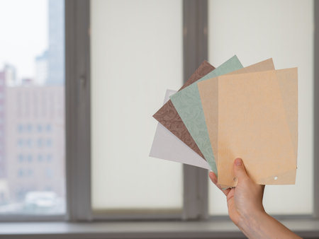 Woman holding fabric samples of roller blinds against window background.の写真素材