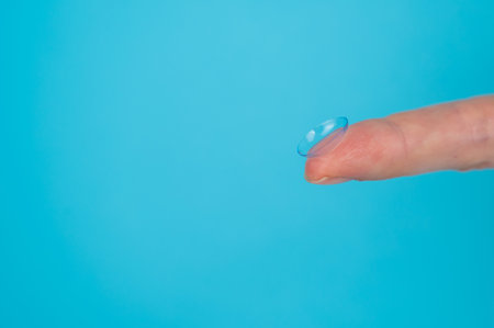 Woman holding contact lens on blue background.の写真素材