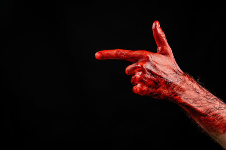 Bloody male hand gesturing shows a gun against black background.の写真素材