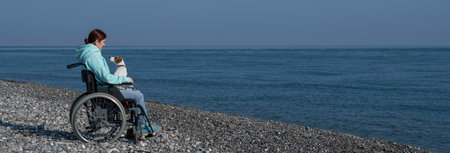 A serene Caucasian woman in a wheelchair is resting on the seashore with a jack russell terrier dog.