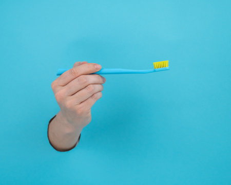 A womans hand sticks out of a blue paper background and holds a toothbrush.の写真素材
