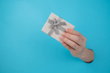 A womans hand sticks out of a blue paper background and a gift box.