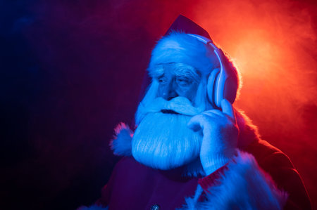 Santa claus listens to music with headphones at a party. Blue red neon light and smoke.の写真素材