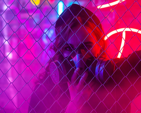 Caucasian woman in a gas mask behind a fence in a neon studio.