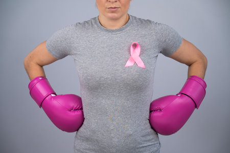 A faceless woman in pink boxing gloves with a pink ribbon holds her hands at her hips. Fight against breast cancer.の写真素材