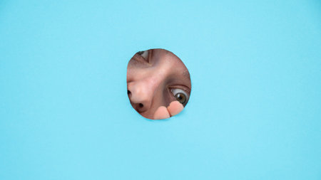 Woman peeking out of hole in blue paper background.の写真素材