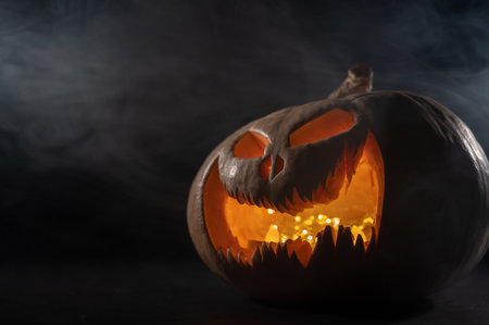 A creepy pumpkin with a carved grimace in the smoke. Jack o lantern in the dark.の写真素材
