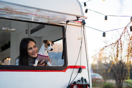 Caucasian woman looks out of the window of the van while hugging her dog Jack Russell Terrier....