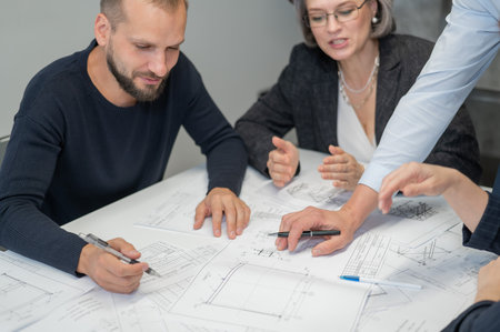 Close-up of the hands of four colleagues with blueprints on the table in the office. Brainstorming of engineers and architects.の写真素材