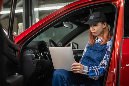 Woman auto mechanic doing diagnostics in car using laptop.の写真素材