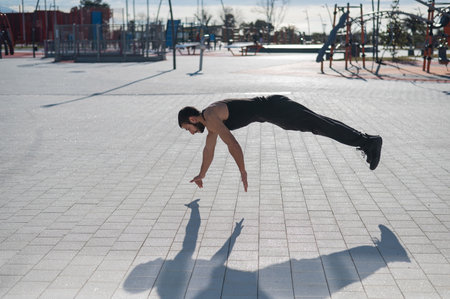A man in black sportswear jumps doing push-ups in the park.の写真素材