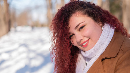 Portrait of a red-haired curly fat woman in the park in winter.