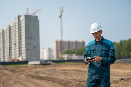 A man in a helmet and overalls controls a drone at a construction site. The builder carries out...