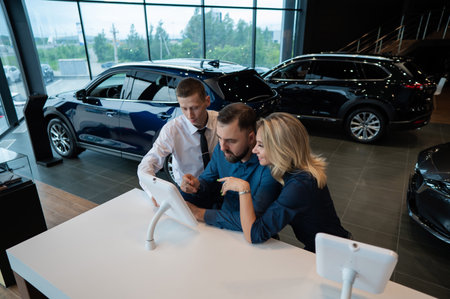 Caucasian married couple chooses a car in a car dealership on digital tablets.の写真素材