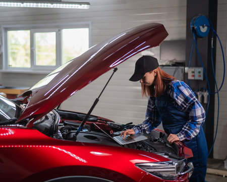 Woman auto mechanic doing engine diagnostics using laptop.の写真素材