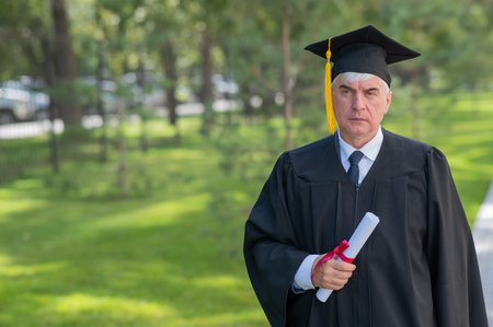 Serious old man in graduation gown holding diploma outdoors.の写真素材