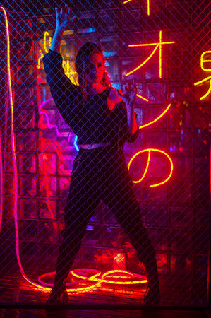 Caucasian woman in neon studio behind chain-link mesh.の写真素材