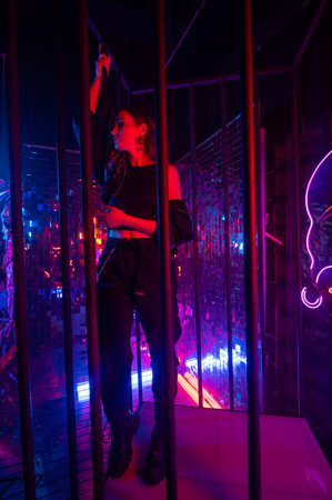 Caucasian woman in neon studio behind steel bars.の写真素材