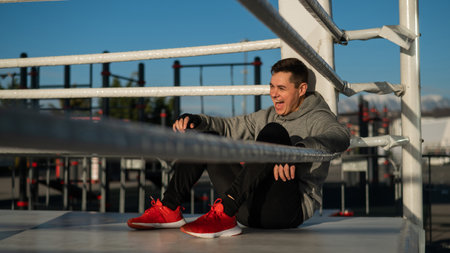Caucasian male boxer resting in the ring outdoors.