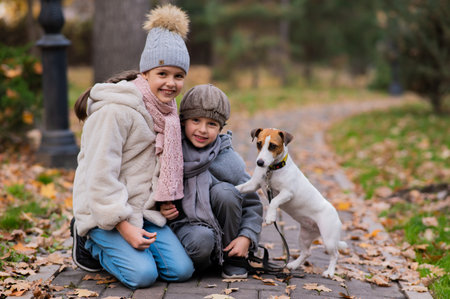 Caucasian boy and girl posing sitting on sidewalk with jack russell terrier dog in park in autumn.の写真素材