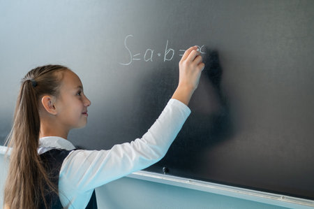 The schoolgirl answers at the lesson. Caucasian girl writes a formula on a blackboard.