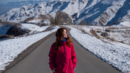 Red-haired caucasian woman in fuchsia-colored jackets in snowy mountains.