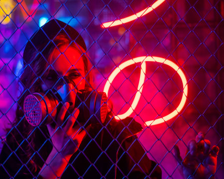 Caucasian woman in a gas mask behind a fence in a neon studio.の写真素材